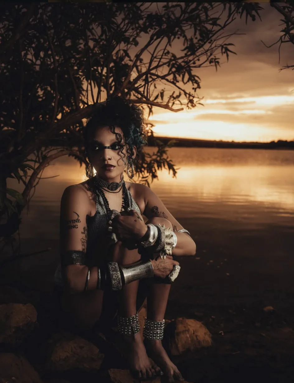 K⭐Y crouched by a lake at sunset, wearing silver jewelry